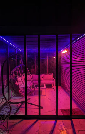 Indoor patio area with pink and purple lighting, featuring a swing chair and sofa.