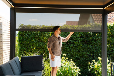 Man adjusting outdoor screen on a pergola with greenery in the background