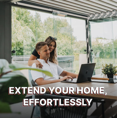Two people working on a laptop in a modern home office with large windows.