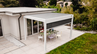 Patio with a retractable pergola over a dining table in a garden setting.