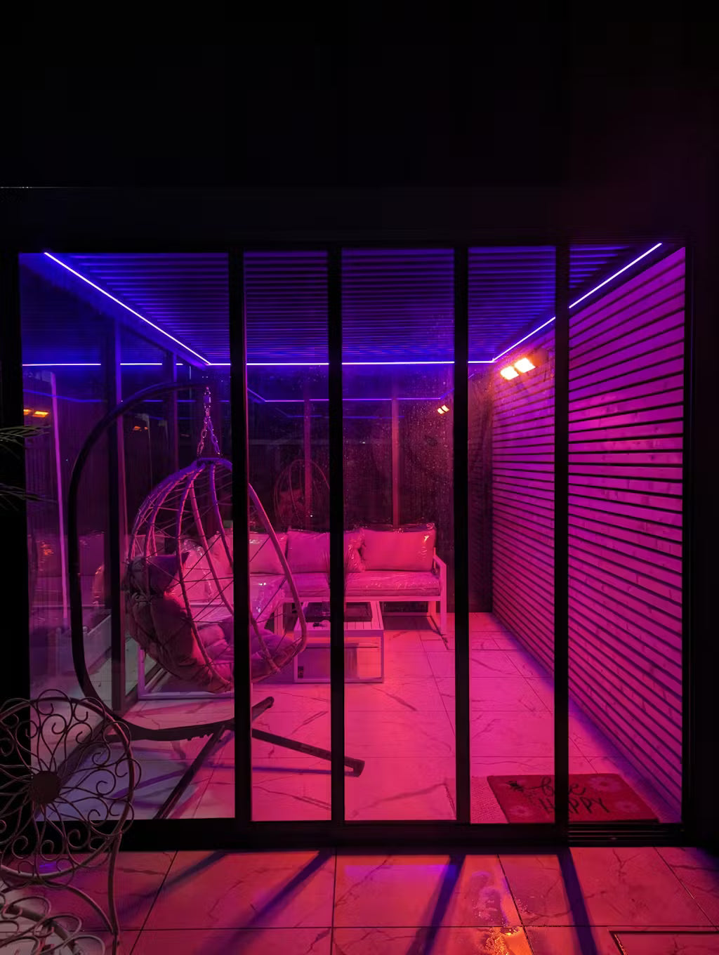 Indoor patio area with pink and purple lighting, featuring a swing chair and sofa.