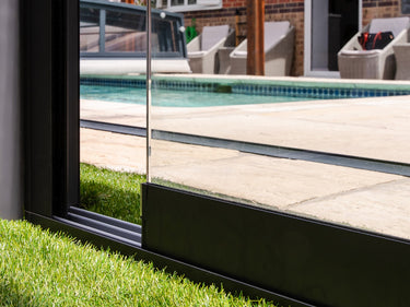 Low angle view of sliding glass wall panel bottom edge on metal track beside pool and green grass