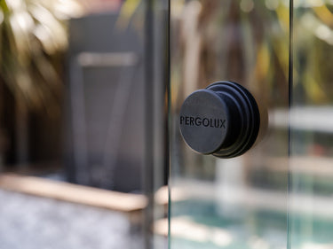 Macro shot of black round magnetic handle on vertical glass pane showing smooth texture and engraved branding