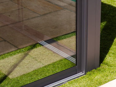 Corner detail of dark grey aluminum frame meeting clear glass panel with slim profile and weather sealing base