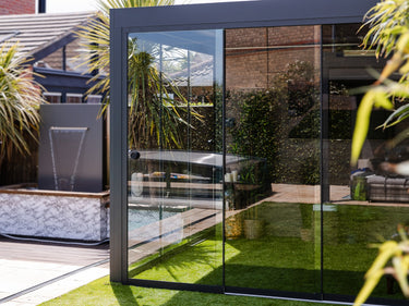 Side view of open sliding tempered glass wall section revealing backyard pool and reflecting palm plants
