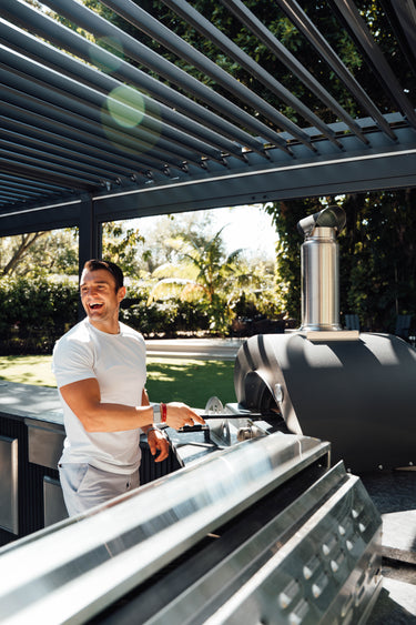 Man grilling outdoors under a pergola with a barbecue in the foreground
