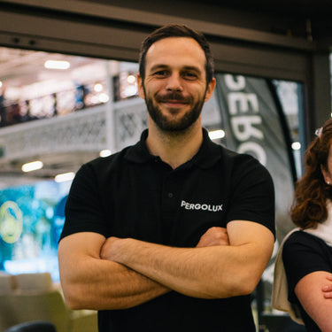 Man wearing a black Pergolux shirt with arms crossed in an indoor setting