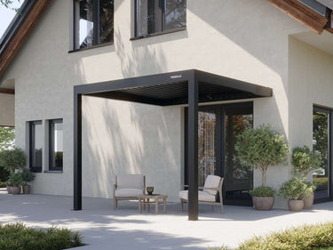 black matte aluminum pergola with PERGOLUX logo shading beige armchairs on paved patio