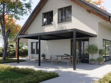 black L-shaped attached pergola shading mixed seating area on stone patio beside wooden fence