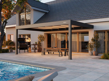 Side view of dark grey motorised aluminium pergola with illuminated light strips and white logo over patio furniture
