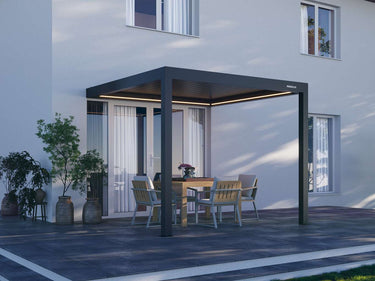 Modern dark grey Pergola 4 Pro attached to wall featuring closed louvres and LED lighting near potted plants