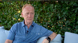 Man in a blue shirt sitting outdoors with greenery in the background