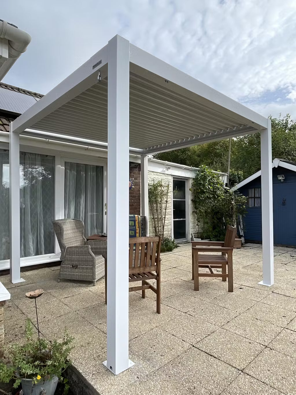 White pergola structure in a backyard setting with patio furniture.