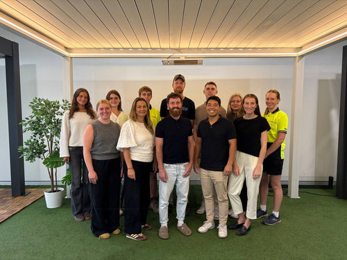 Group of australian people posing for a photo in an indoor setting under a pergola with a plant and modern decor.