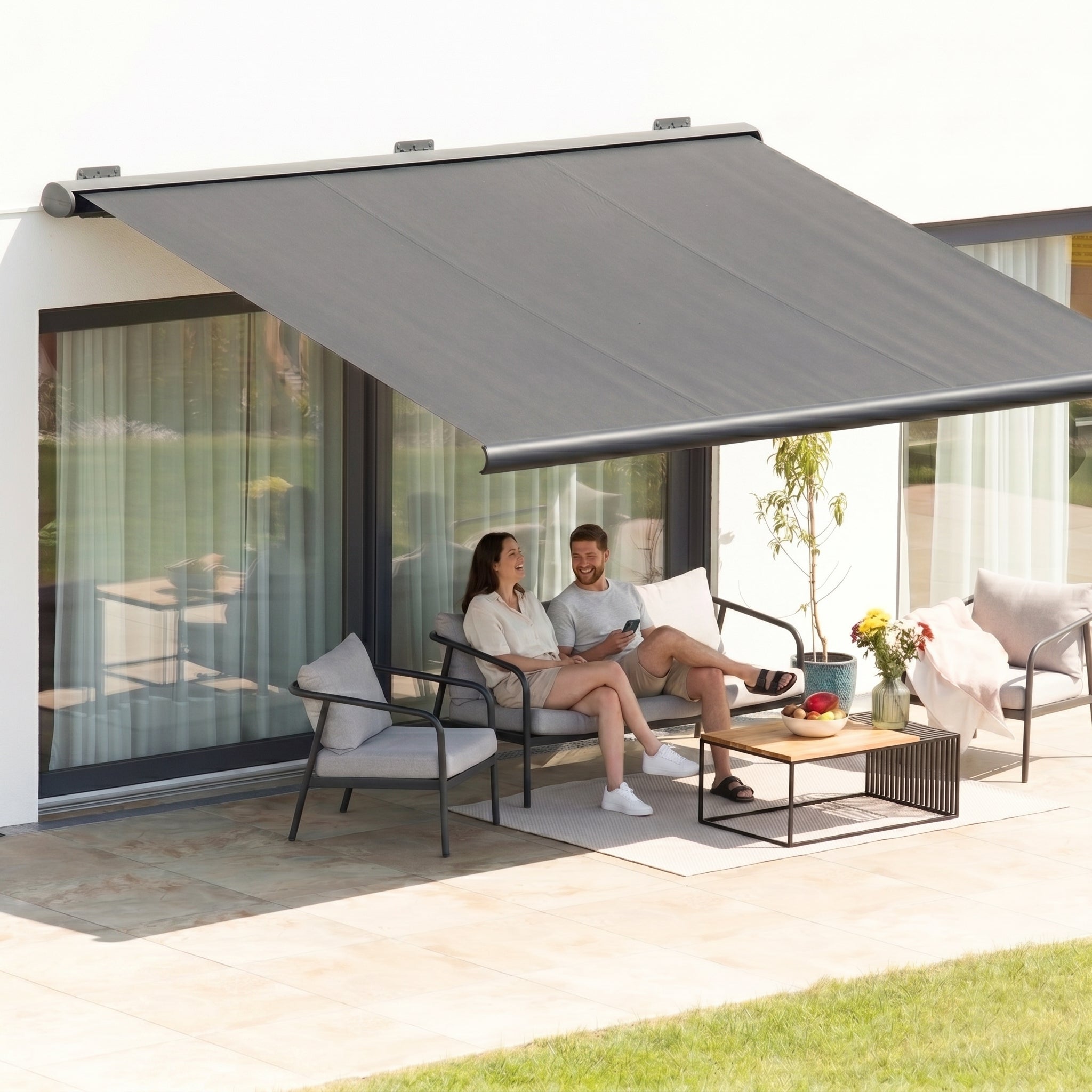 Dark grey angled fabric awning providing shade for couple seated on grey sofa on tiled deck