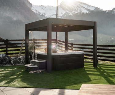 dark brown cubic pergola sheltering hot tub on artificial turf with mountain backdrop