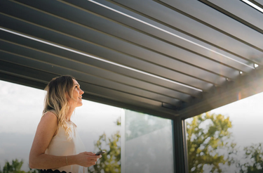 Low angle view of open adjustable aluminium louvres allowing daylight through with woman holding remote control