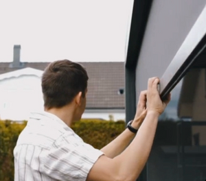 Person opening a pergola screen with a house in the background