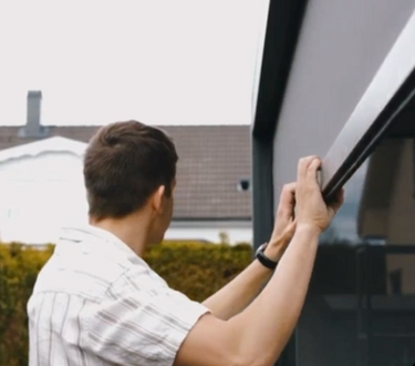 Person opening a pergola screen with a house in the background