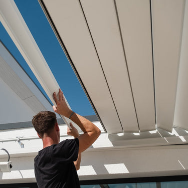 Installing white louvered pergola blades with mounting brackets against blue sky