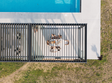 Top-down view of a pool with a pergola fence and chairs on a grassy area.