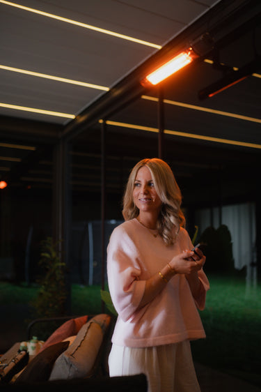 Woman using remote under night pergola with active bright orange infrared heating lamp and linear ceiling lights
