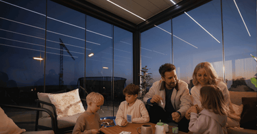 Family gathering under PERGOLUX Pergola 4 Pro Max transparent side panels with linear LED ceiling lights at twilight