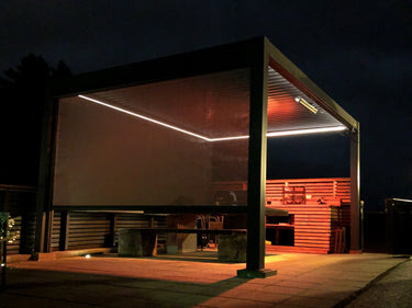 White LED light strips along dark metal pergola gutter rails casting glow over outdoor furniture
